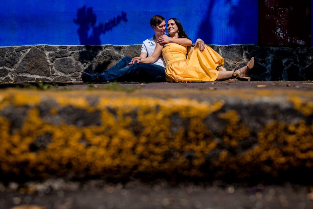 a couple is sit together and hugging each other, they are sit on the floor in front of frida kahlo museum in cdmx