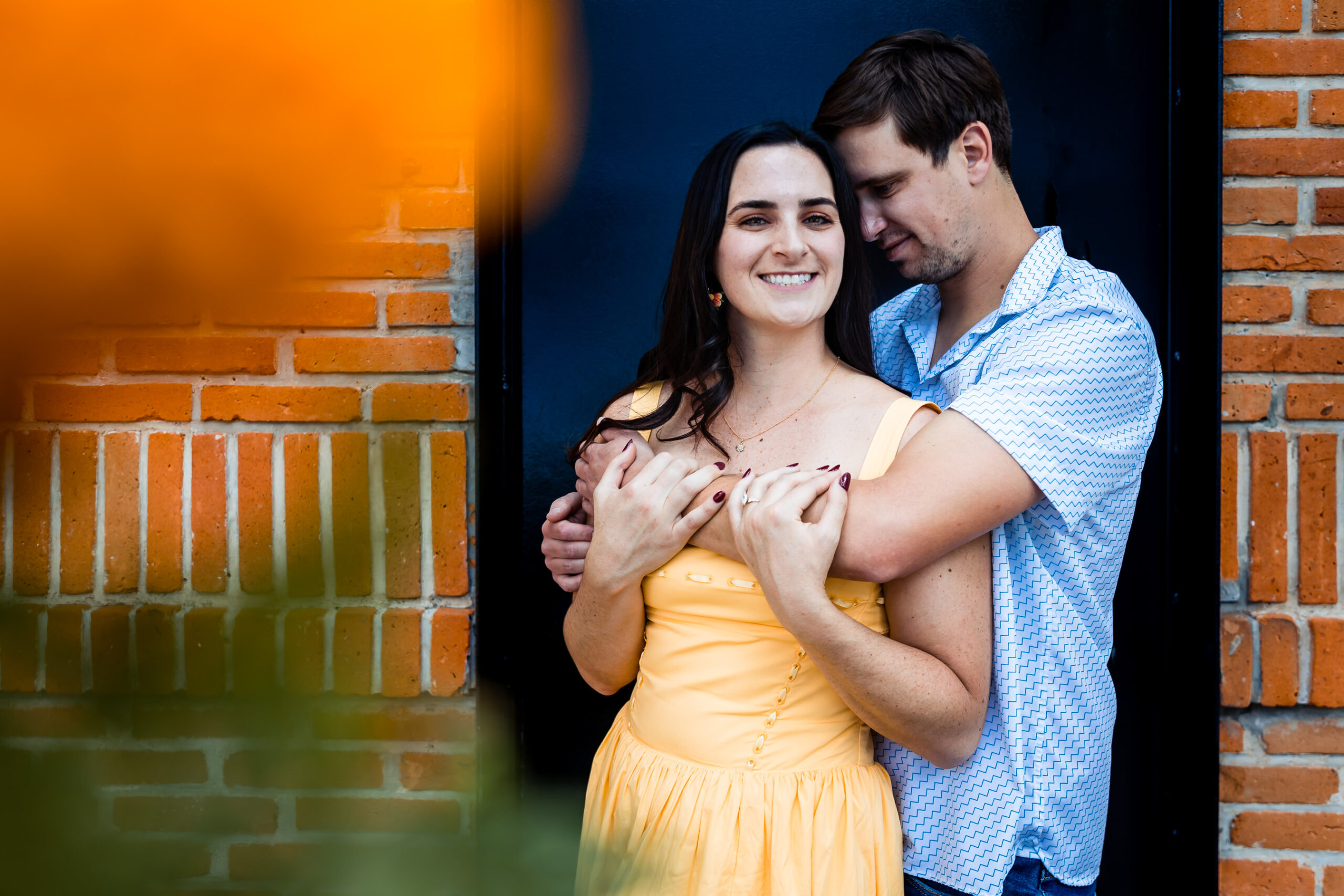girl and boy hugging in front of a black door in cdmx, girl smile and a orange flower on the side