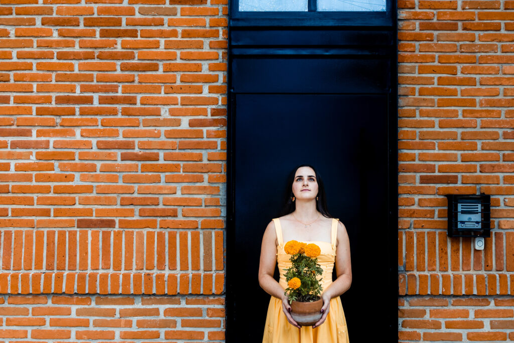 a girl is in front of a door in coyoacan cdmx, she is holding a plants with orange flowers