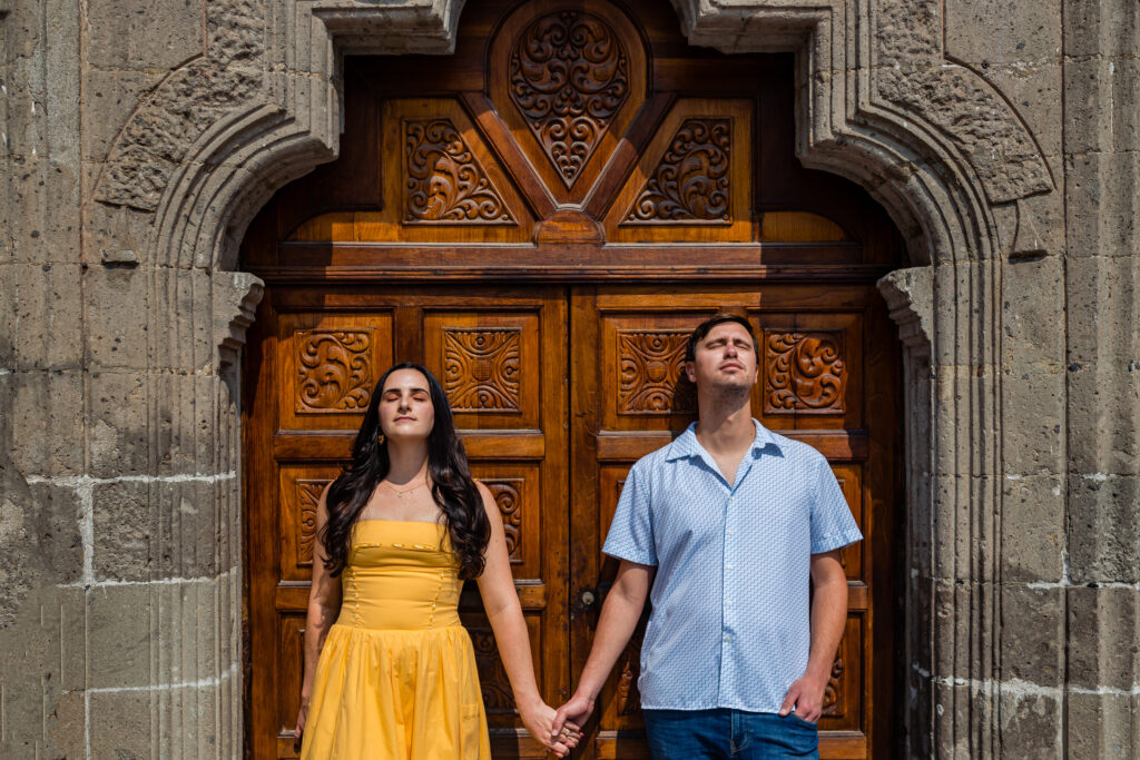 couple is holding hands and looking to the sun with the eyes close in front of an amazing wood door