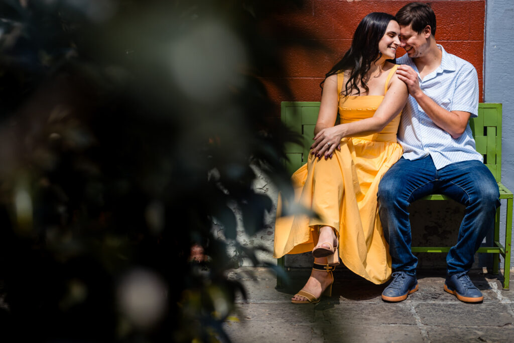 a couple is sit on a bench they are hugging each other and smile together touching their front heads and have a nice moment