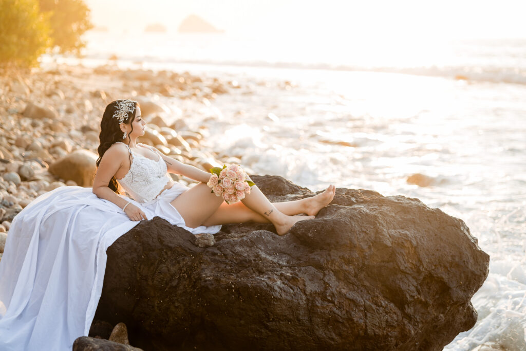 bride are sitting on a rock with the ocean in the background and a nice warm orange light, the bride is holding a bouquet