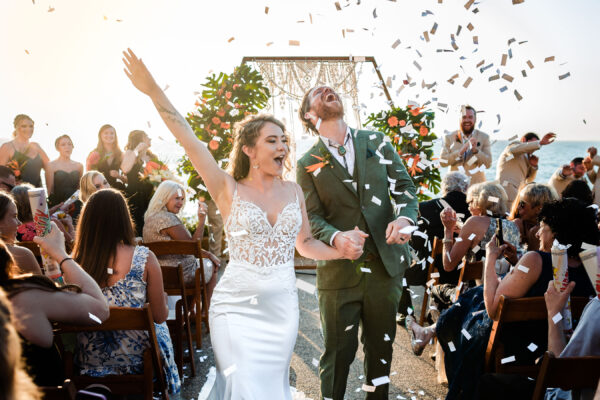 couple walking and smiling at the end of their wedding ceremony with the ocean o nthe background