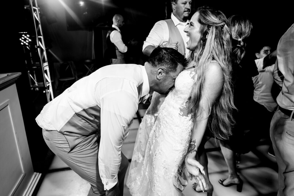 bride and groom dancing on the dance floor during their wedding day, the groom have his face on the chest of the bride, funny moment