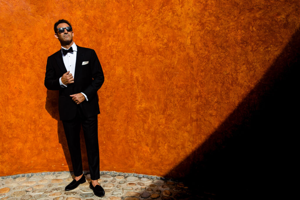 groom with a black suite and sun glasses on a orange wall on his wedding day