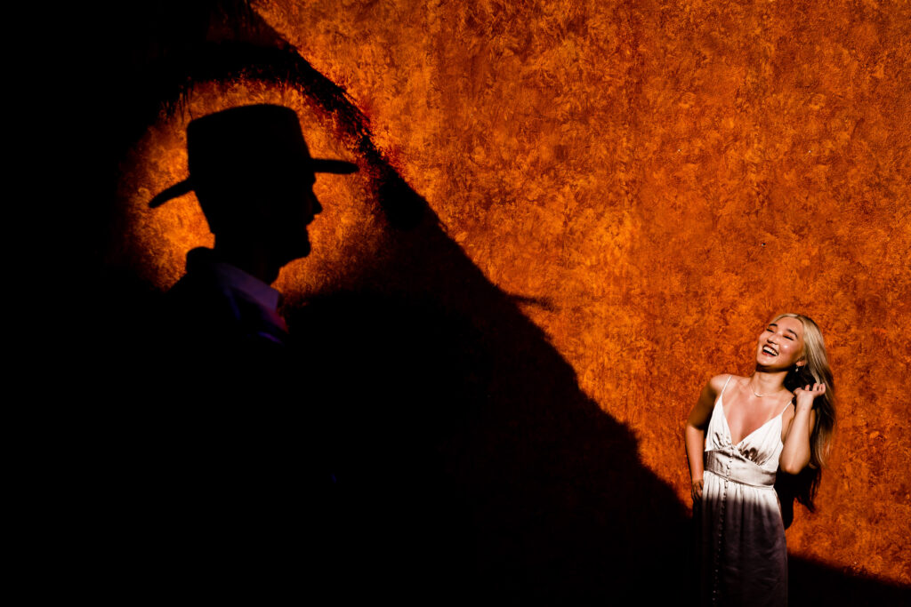 siluetee of a groom in the foreground and on the background a bride is smiling