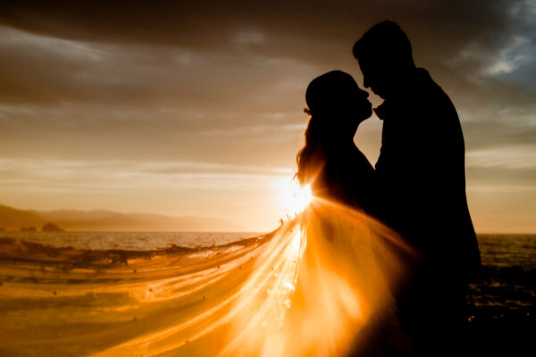 couple is hug each other during sunset time, they are on a siluette and the veil have light on it from the sun