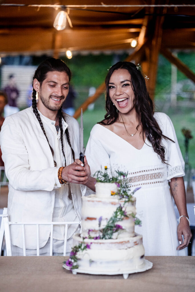 bride and groom are holding a knife during the cutting cake, the bride is smiling hand playing with the knife
