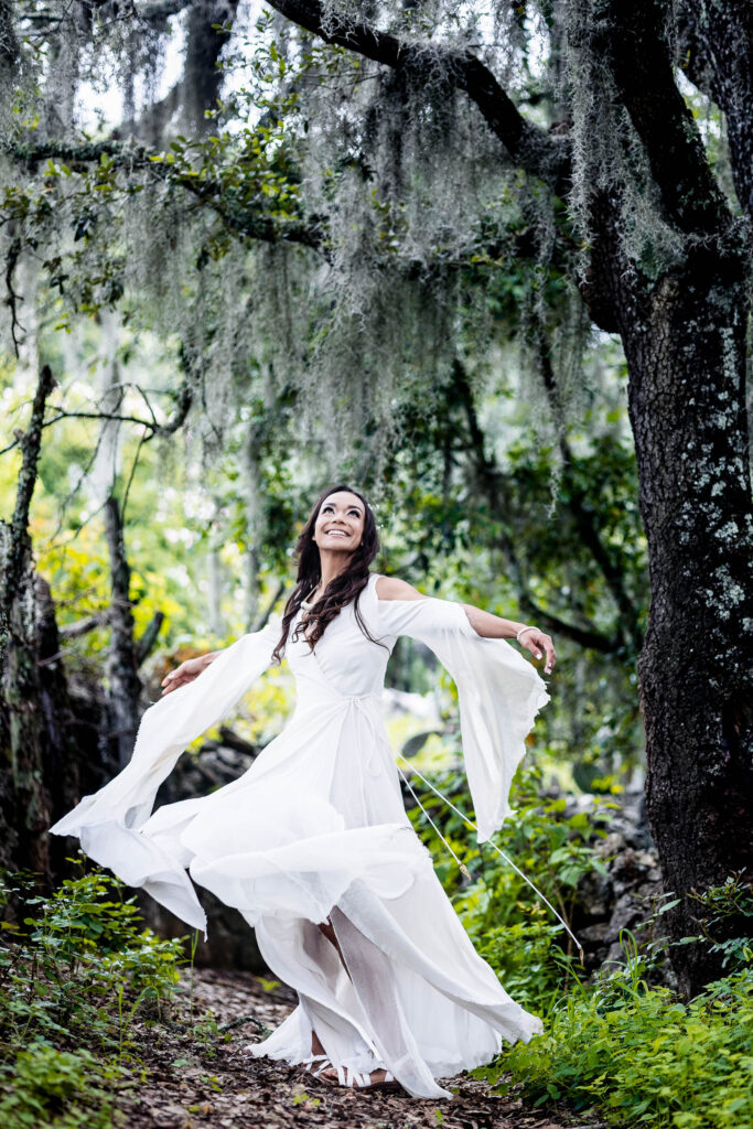 the bride is in a green forest, looking up and smiling...she is turning on her self and the dress is moving on a magical way