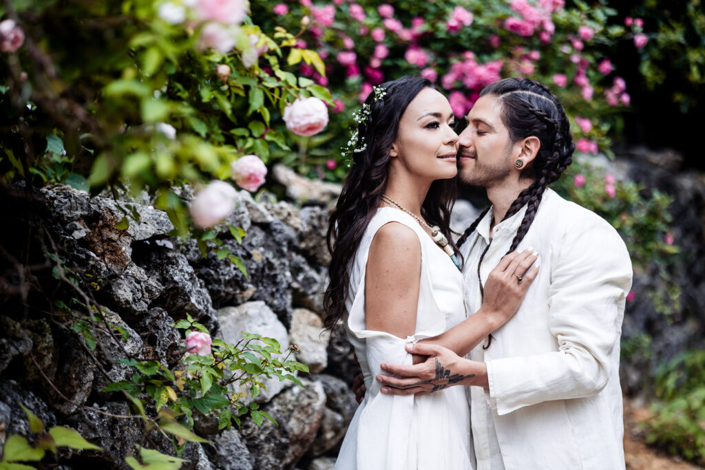 bride and groom are hugging each other, the groom is looking to her and on the background they have nice pink roses